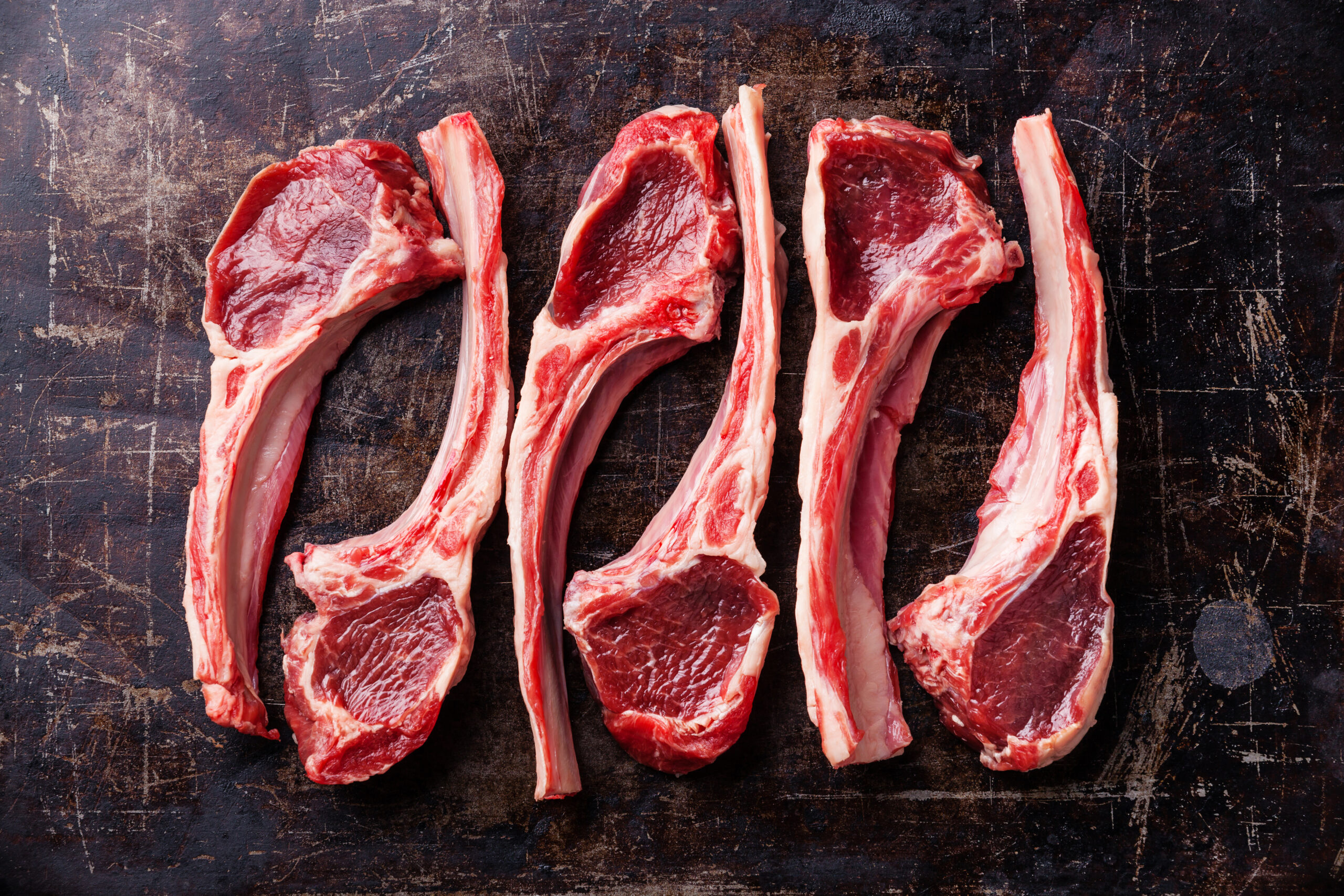 Raw fresh lamb ribs on dark background Block of butter on parchment paper with sliced pieces, placed on a wooden cutting board, surrounded by a light-colored cloth and a knife. Ideal for cooking and baking.